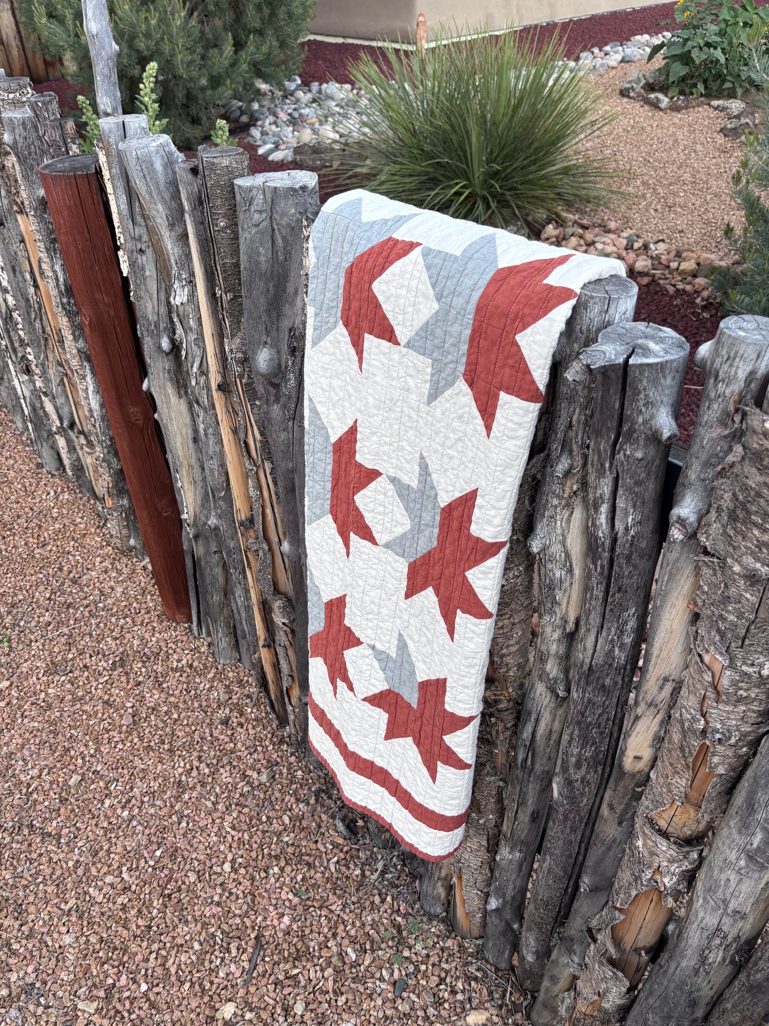 Quilt with red and blue star pattern draped over a wooden fence outdoors.