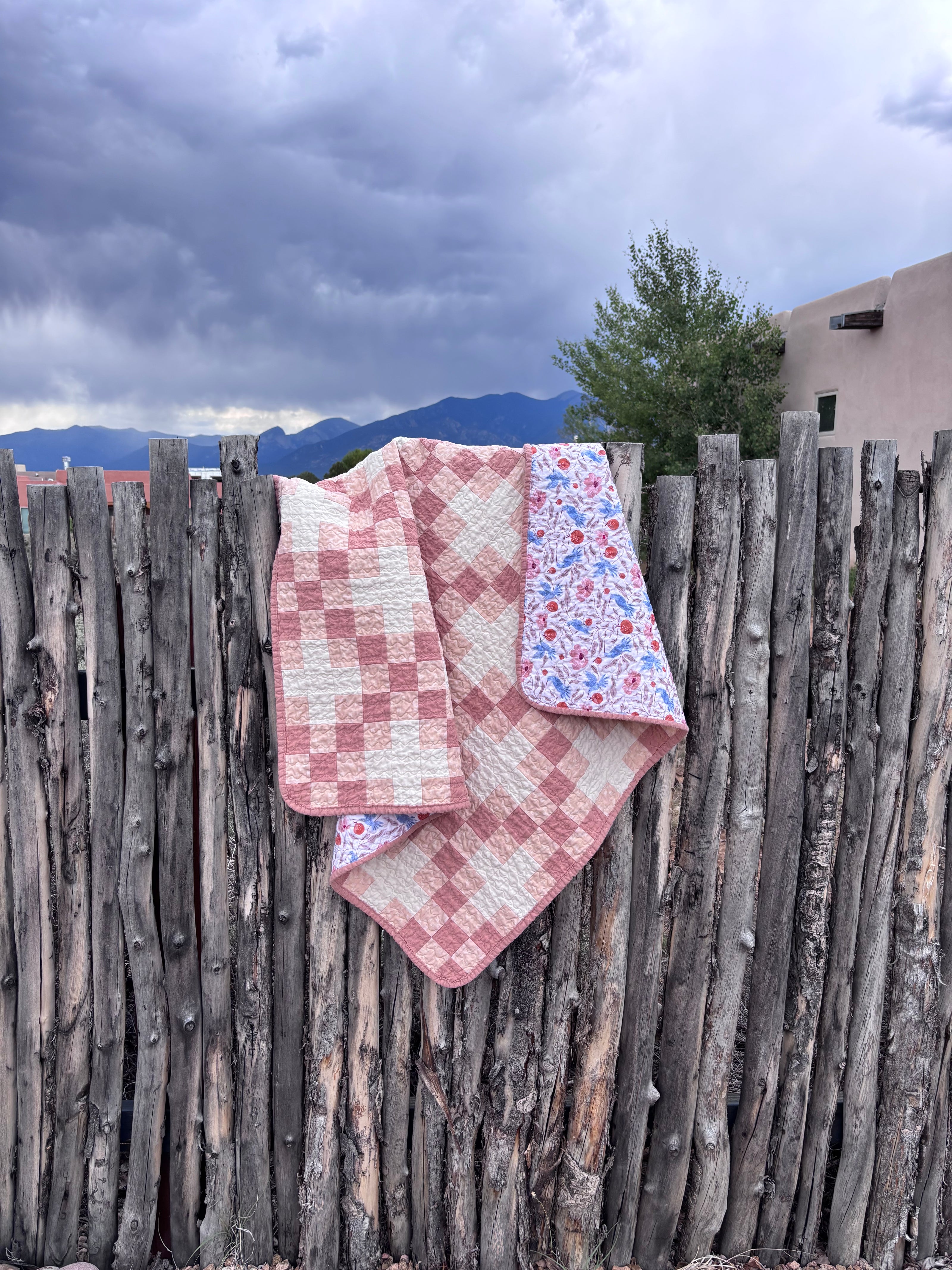 A baby quilt with pink and white squares draped over a fence.