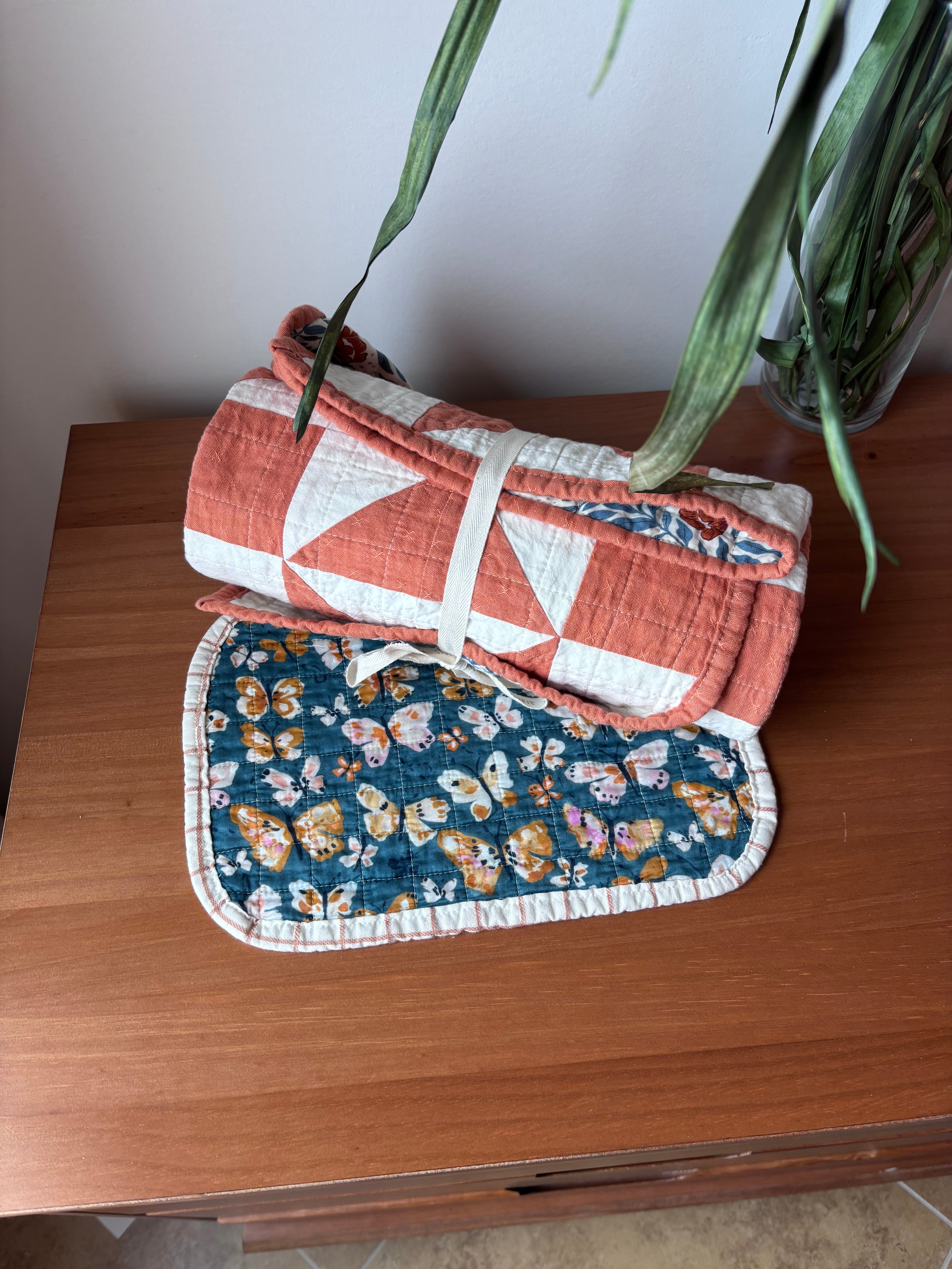 Rolled quilt and baby burp cloth on a wooden surface with a plant in the background
