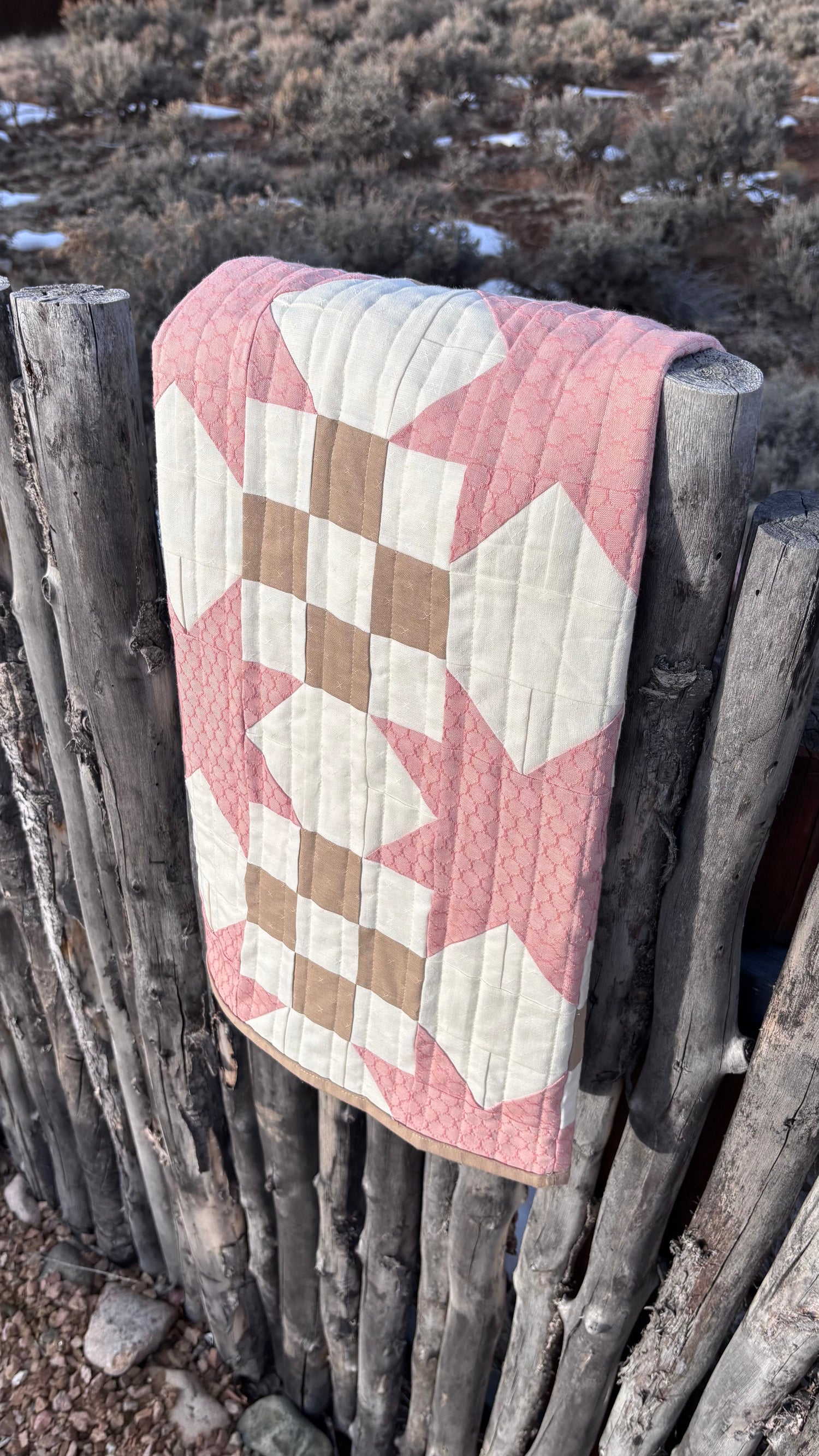 Quilt with star pattern draped over a wooden fence in a natural setting
