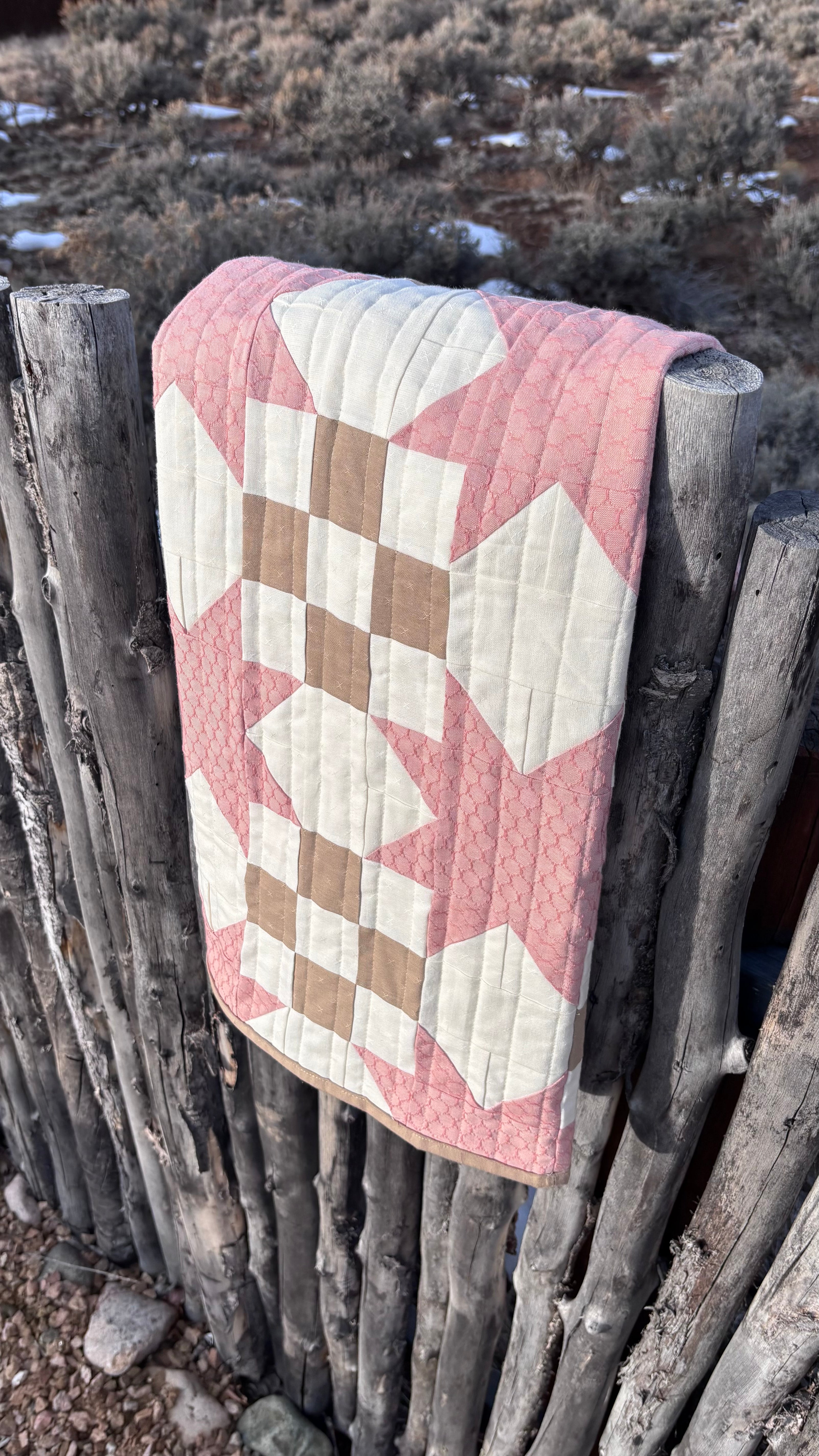 Quilt with star pattern draped over a wooden fence in a natural setting