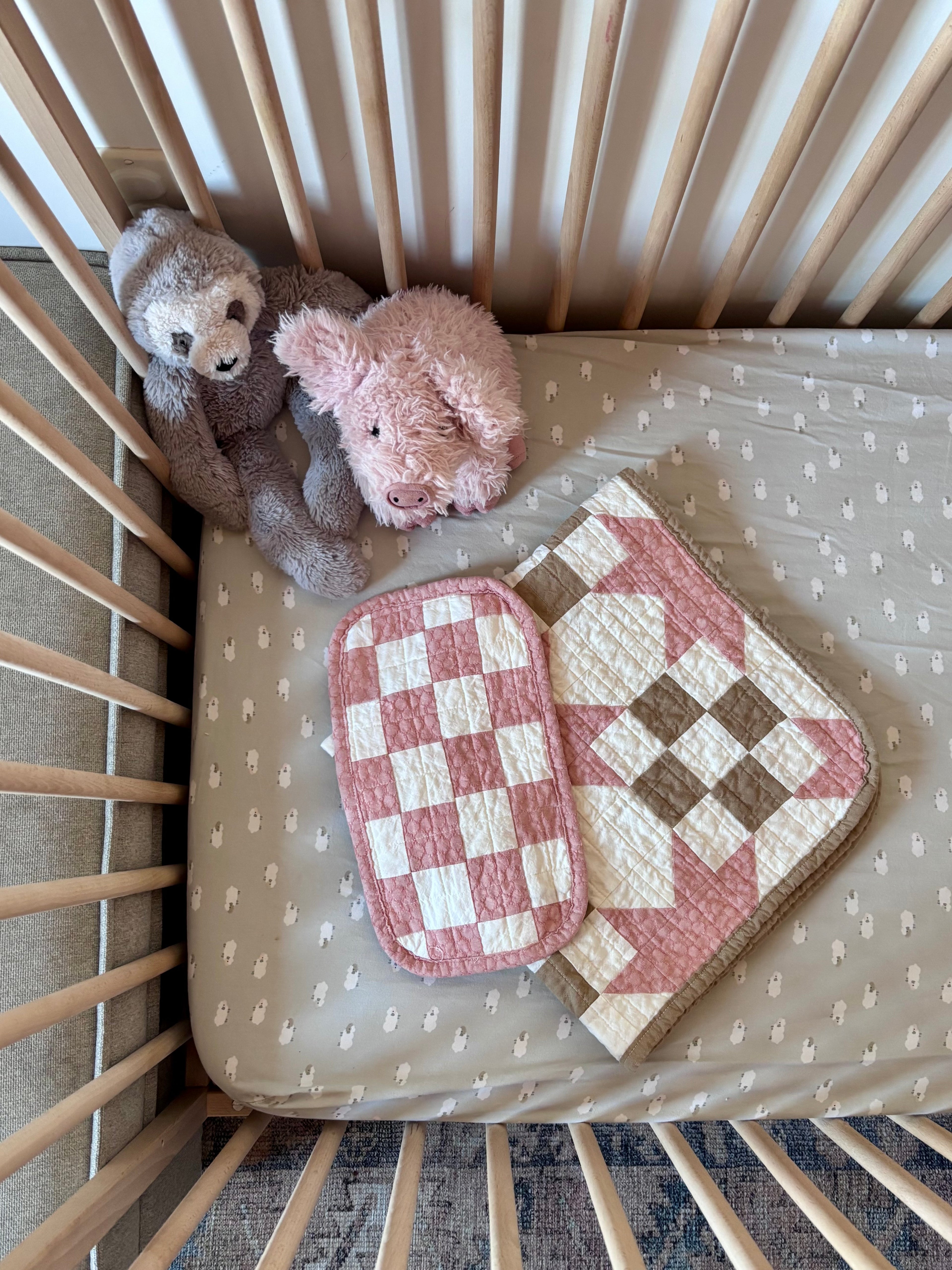 Two teddy bears and two checkered blankets in a crib with a patterned mattress cover.