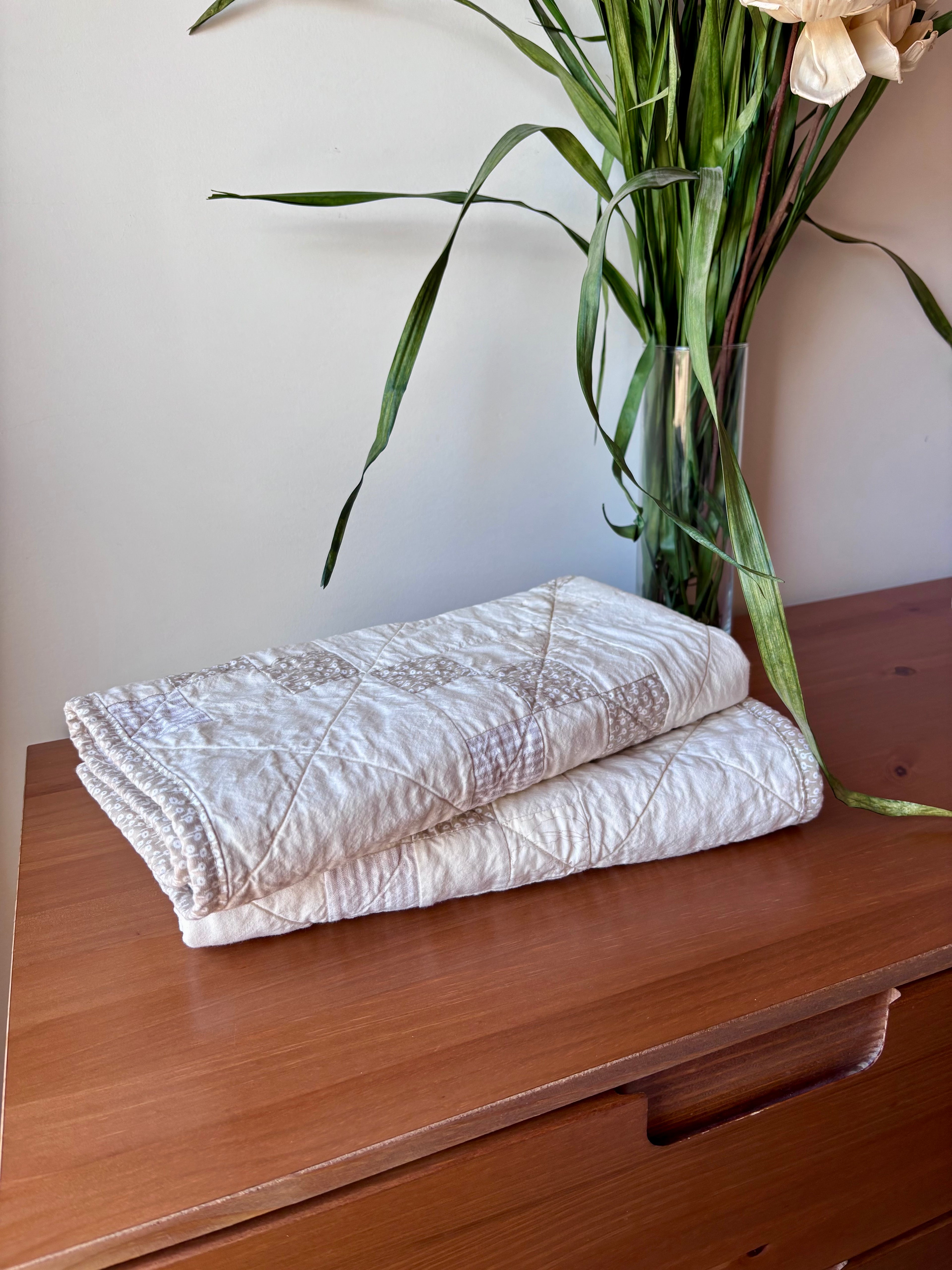 Folded quilt on a wooden surface with a vase of flowers in the background