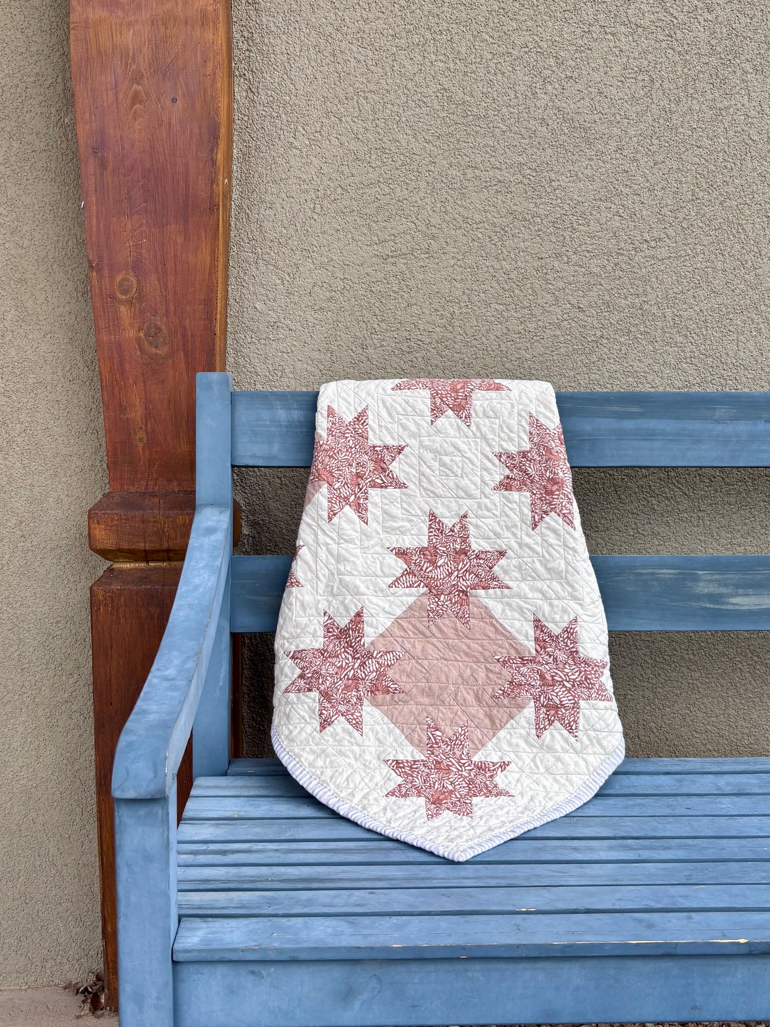 Star-patterned quilt draped over a blue bench against a beige wall.