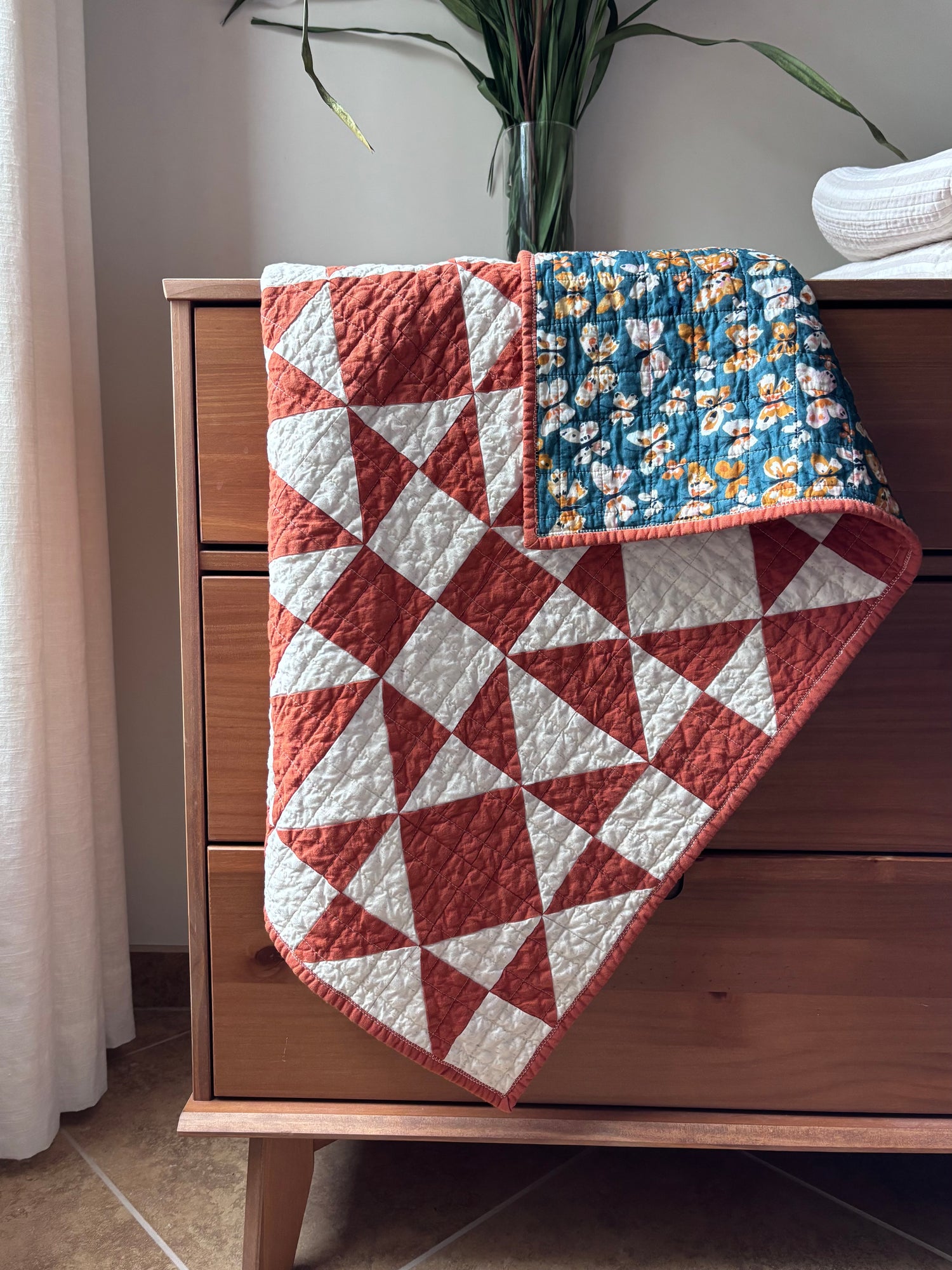 Geometric baby quilt draped on a wooden dresser.